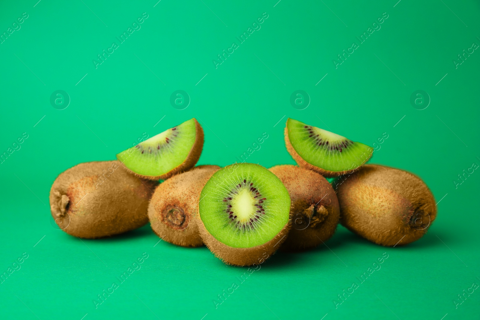 Photo of Heap of whole and cut fresh kiwis on green background