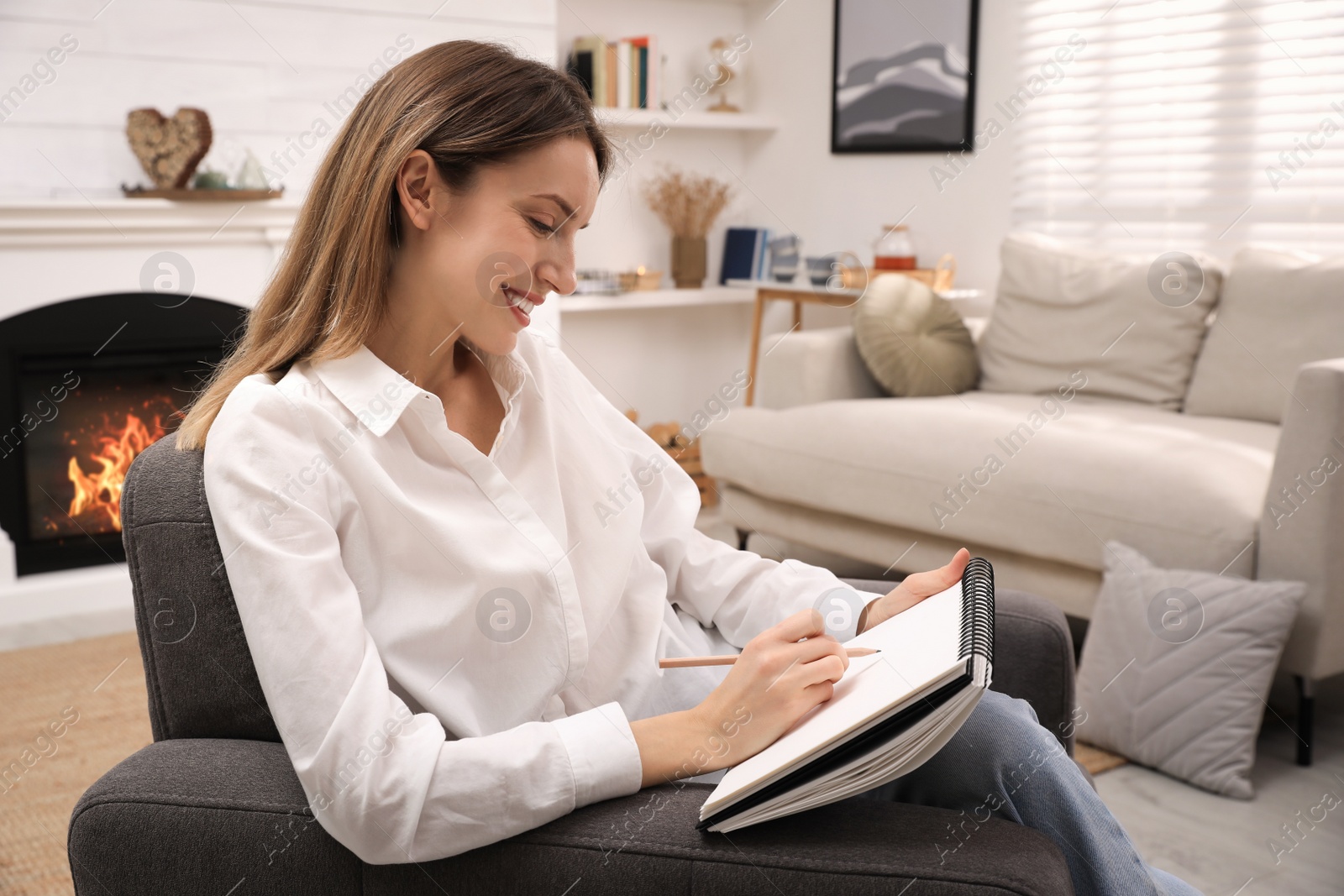 Photo of Young woman drawing in sketchbook with pencil at home