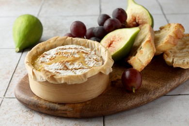 Photo of Tasty baked brie cheese and products on light tiled table