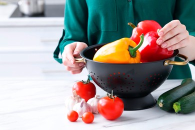 Woman taking bell pepper from black colander at white marble table in kitchen, closeup. Space for text