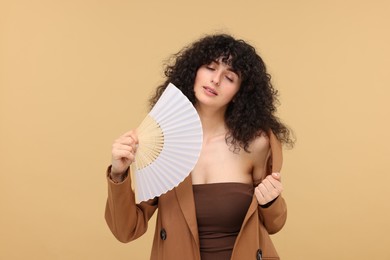 Woman with hand fan suffering from heat on beige background