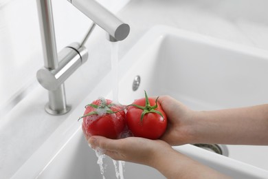 Photo of Woman washing fresh ripe tomatoes under tap water in kitchen, closeup