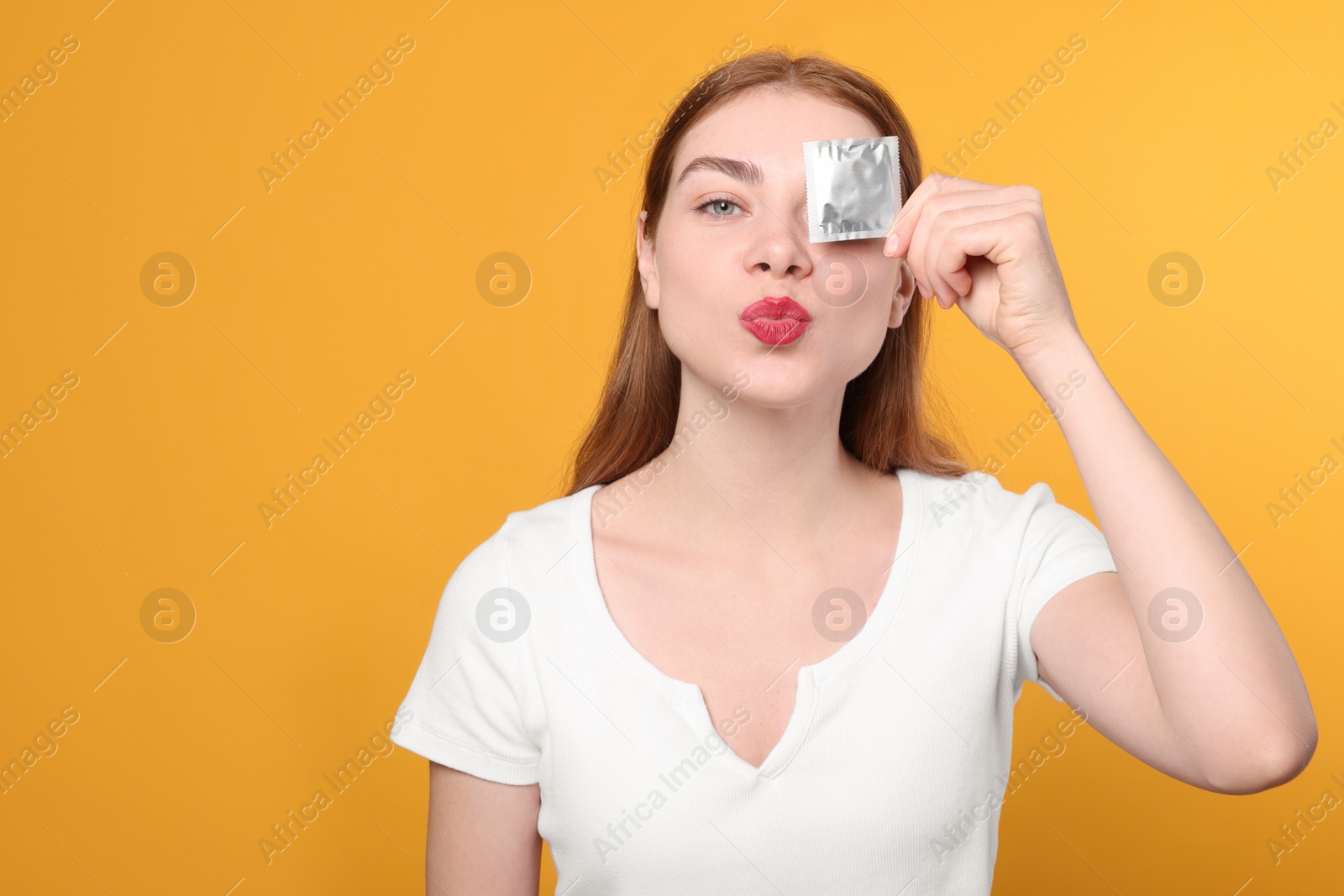 Photo of Woman holding condom on yellow background. Safe sex