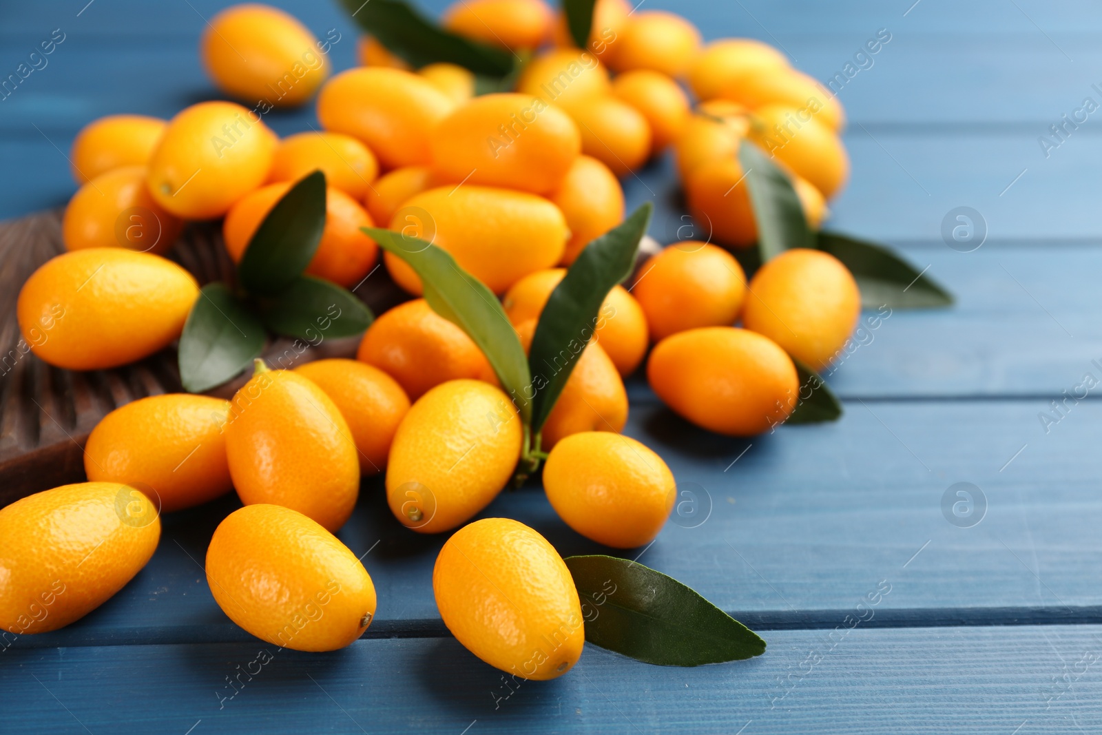 Photo of Fresh ripe kumquats and leaves on blue wooden table, closeup