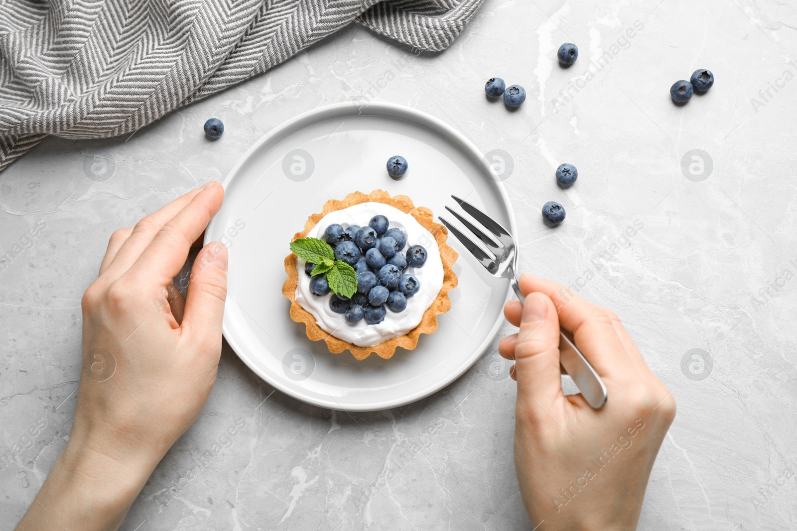 Photo of Woman eating blueberry tart at marble table, top view. Delicious pastries