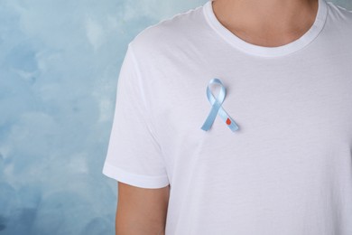 Photo of Man with light blue ribbon and paper blood drop on color background, closeup. World Diabetes Day