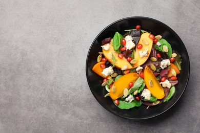 Delicious persimmon salad with pomegranate and spinach on light gray textured background, top view. Space for text