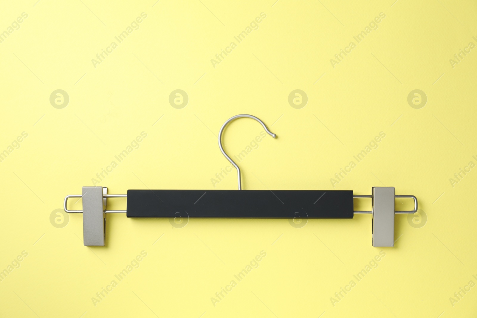 Photo of Empty hanger with clips on yellow background, top view