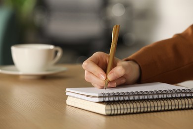 Photo of Woman writing in notebook at wooden table, closeup. Space for text