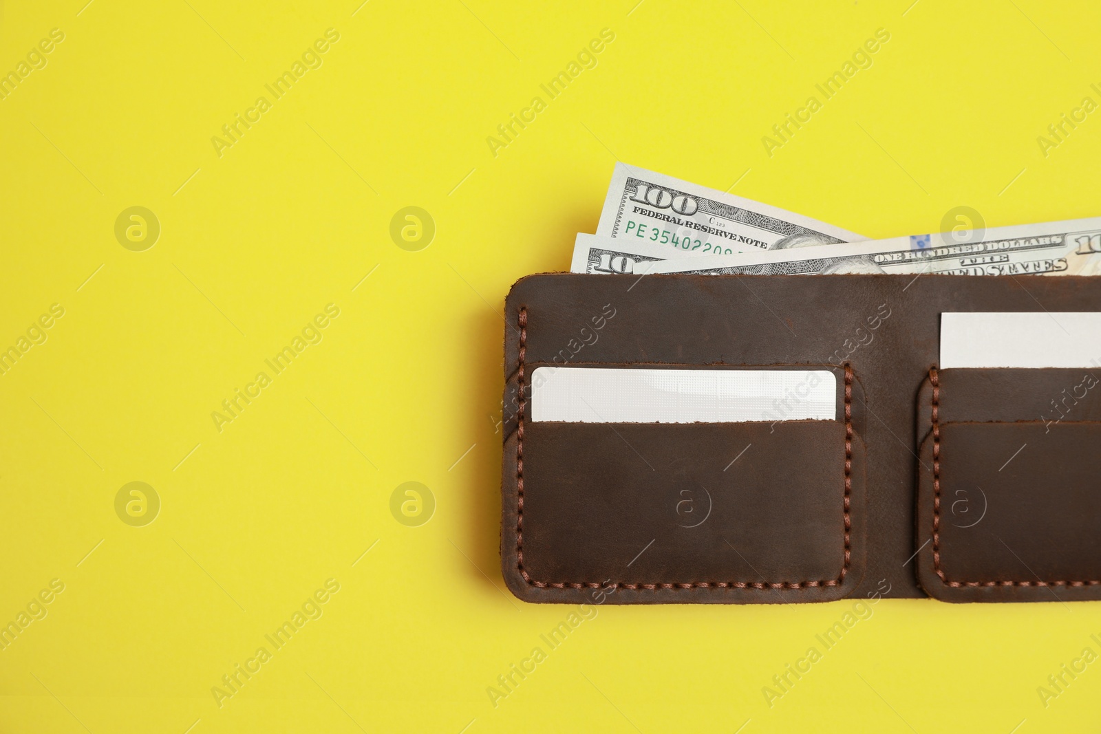 Photo of Stylish brown leather wallet with dollar banknotes on yellow background, top view. Space for text