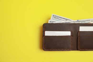 Photo of Stylish brown leather wallet with dollar banknotes on yellow background, top view. Space for text