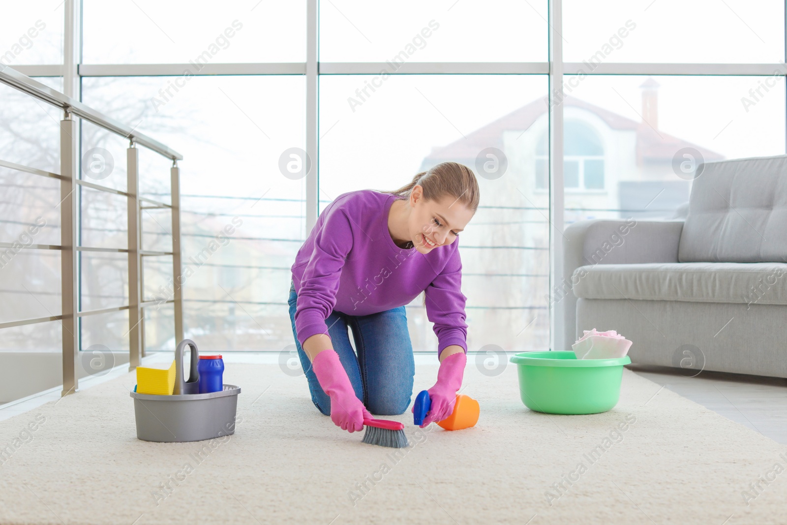 Photo of Young woman cleaning carpet at home