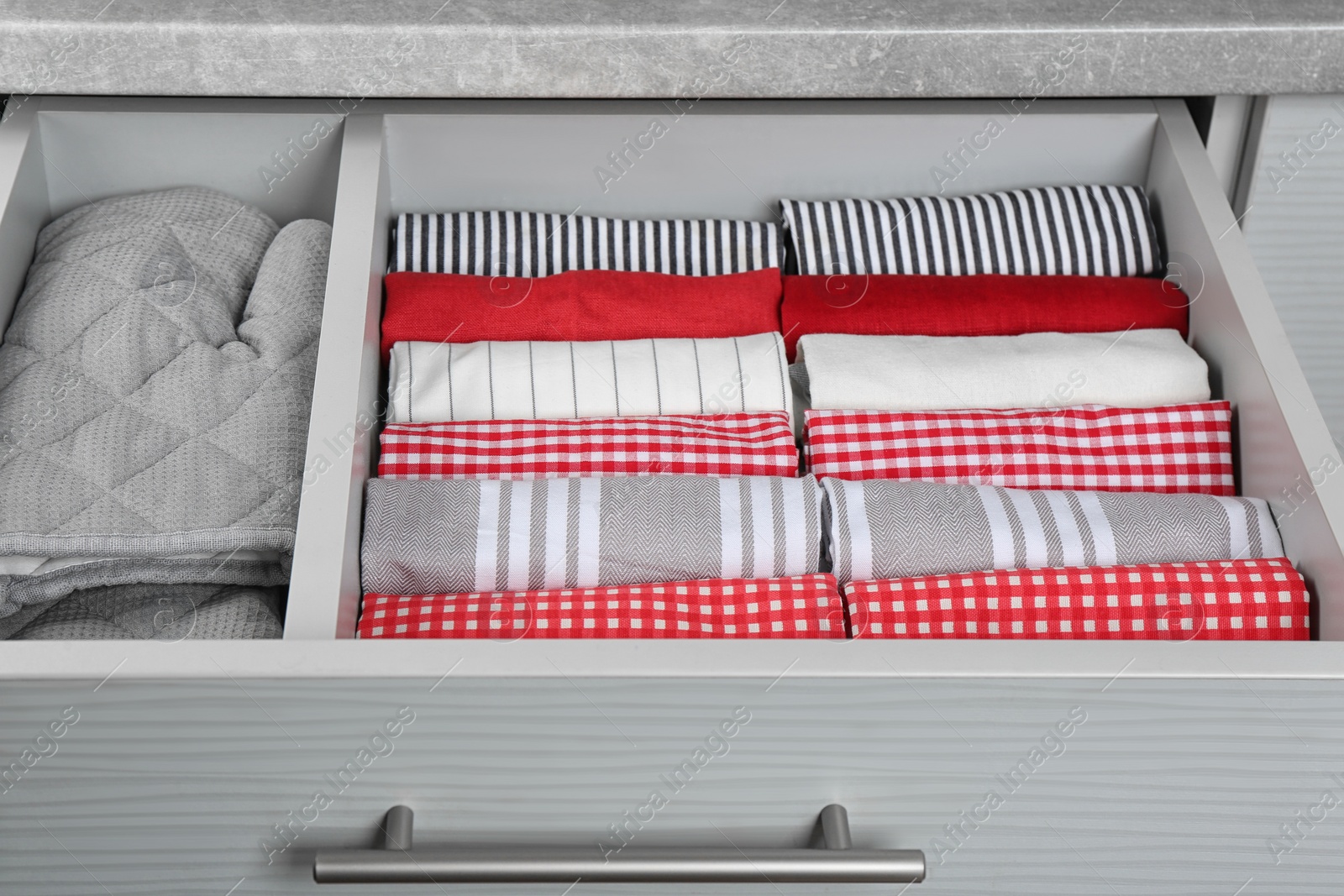 Photo of Open drawer with folded towels and oven mittens. Order in kitchen