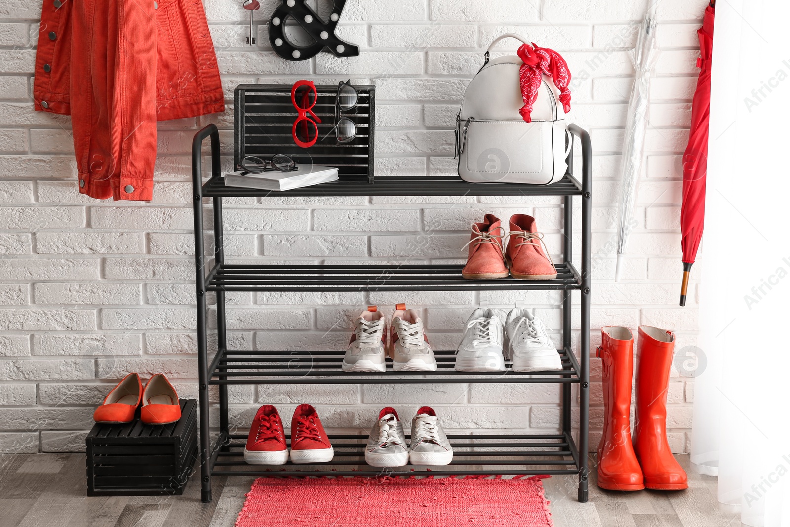 Photo of Shelving rack with stylish women's shoes and accessories near white brick wall indoors