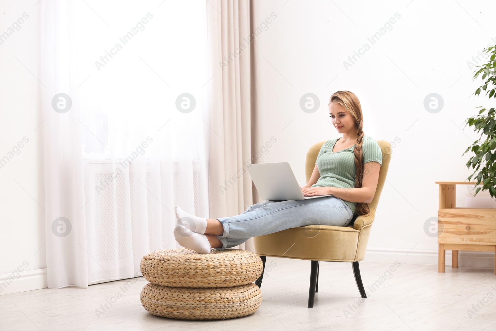 Photo of Young woman with laptop sitting in armchair at home