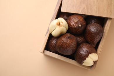 Wooden crate with fresh salak fruits on beige background, top view. Space for text