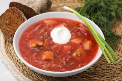 Photo of Tasty borscht with sour cream served with green onion on white table, closeup