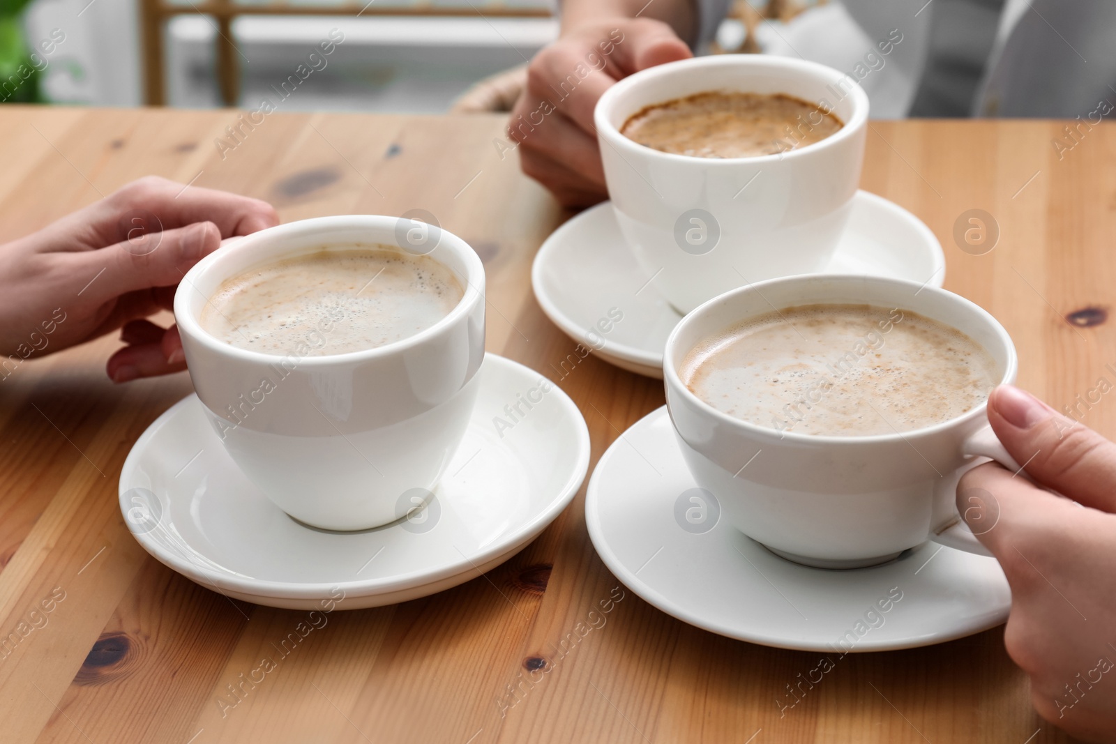 Photo of Women with cups of coffee at table in cafe, closeup