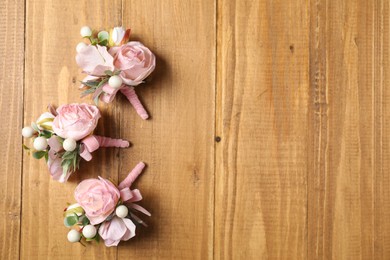 Photo of Stylish pink boutonnieres on wooden table, flat lay. Space for text