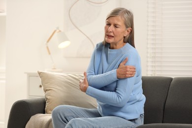 Mature woman suffering from pain in arm on sofa at home. Rheumatism symptom