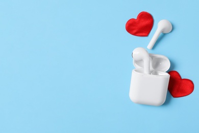 Photo of Modern earphones and red hearts on light blue background, flat lay with space for text. Listening love music songs
