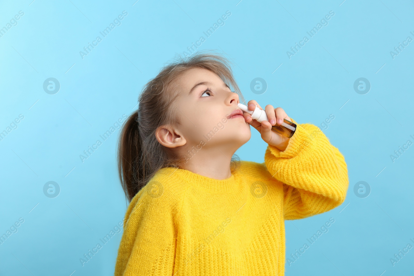 Photo of Sick little girl using nasal spray on light blue background