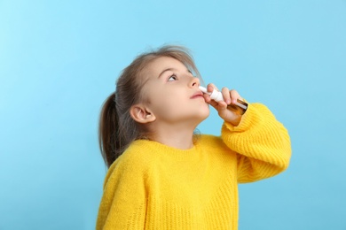 Photo of Sick little girl using nasal spray on light blue background