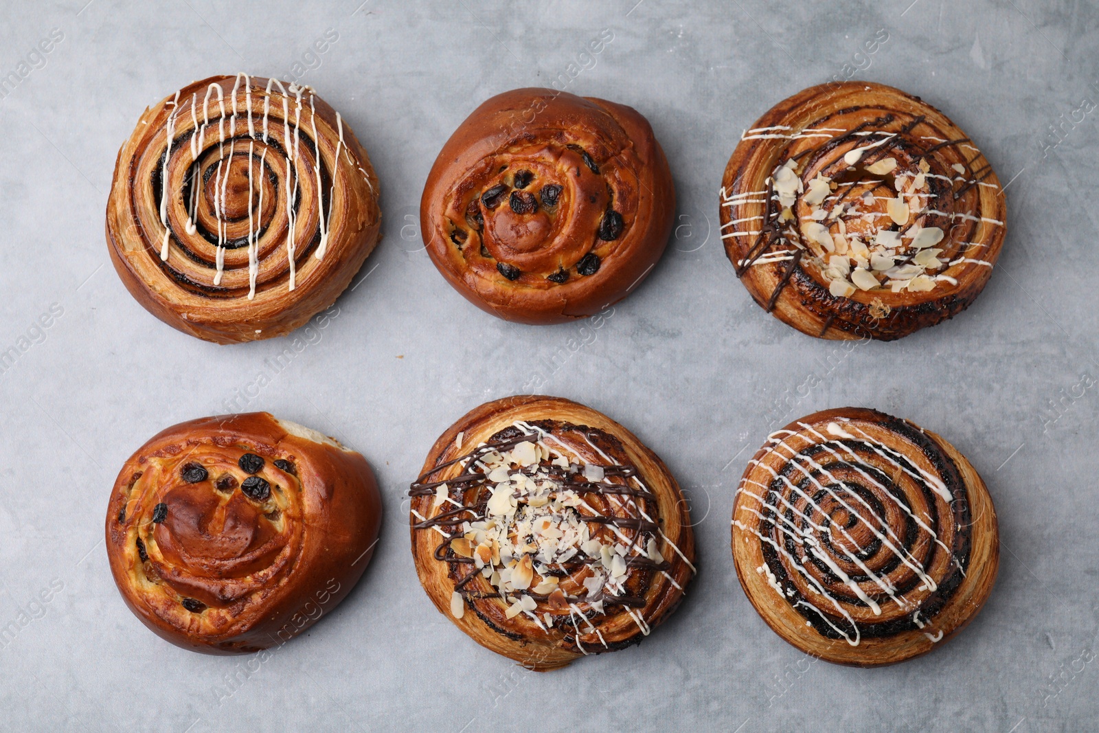 Photo of Different delicious rolls on light grey table, flat lay. Sweet buns