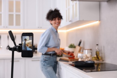 Photo of Food blogger cooking while recording video in kitchen, focus on smartphone