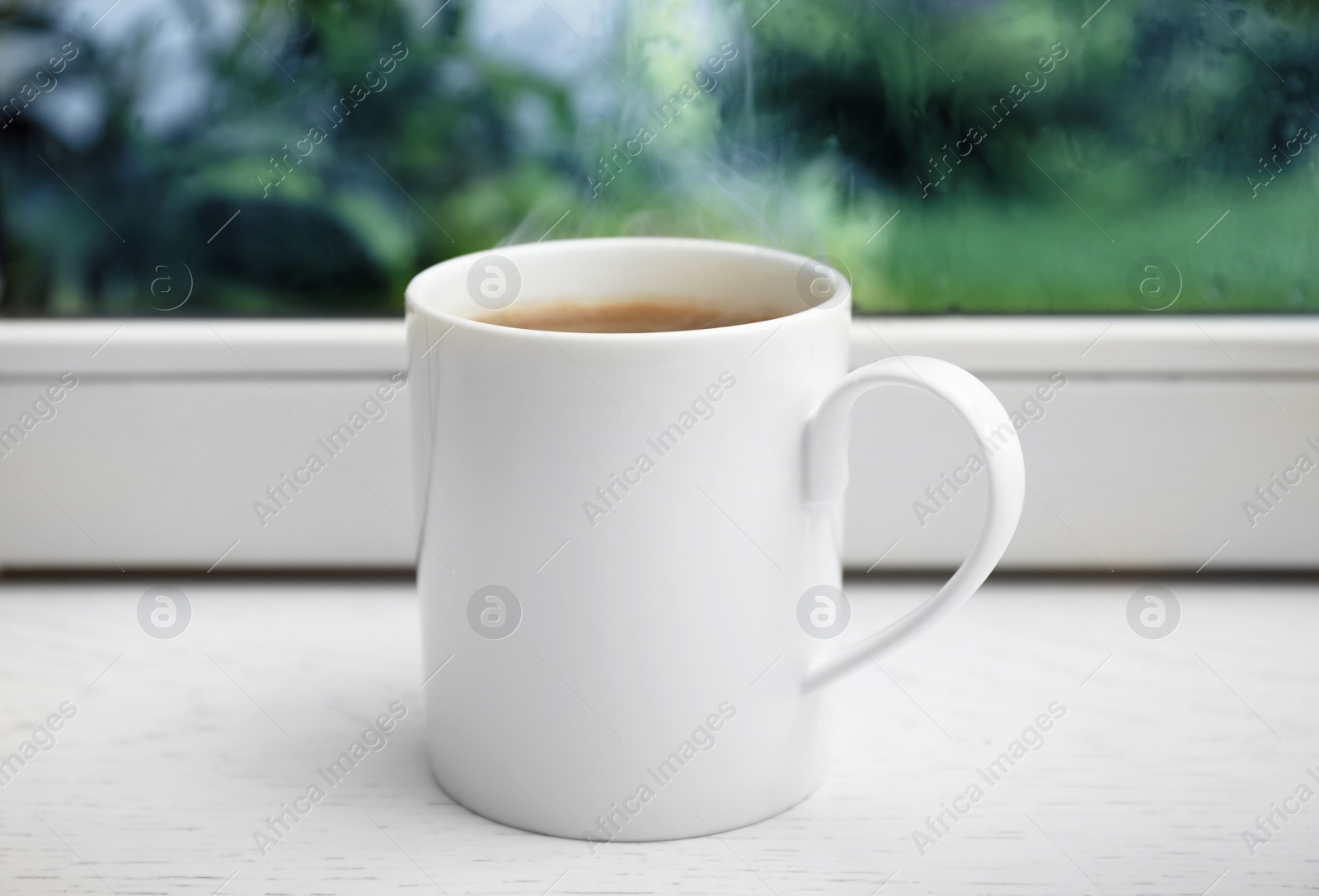 Photo of Cup of hot coffee on white wooden windowsill