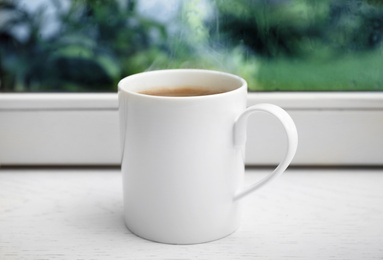 Photo of Cup of hot coffee on white wooden windowsill