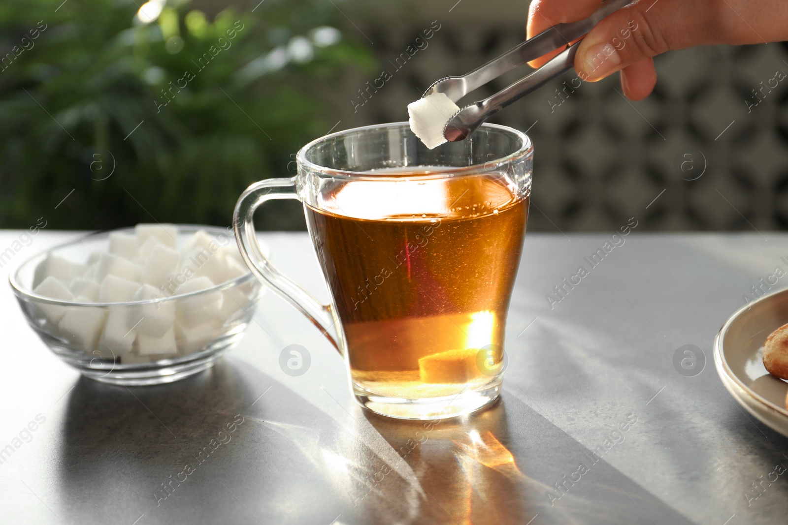 Photo of Woman adding sugar cube into cup of tea at dark table, closeup