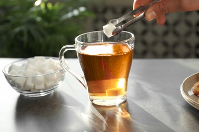 Photo of Woman adding sugar cube into cup of tea at dark table, closeup