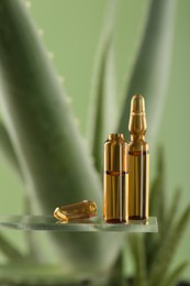 Skincare ampoules near aloe vera on light green background, closeup