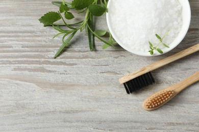 Photo of Toothbrushes, green herbs and sea salt on wooden table, flat lay. Space for text