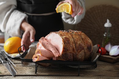 Photo of Woman squeezing juice from orange slice onto delicious baked ham at wooden table, closeup