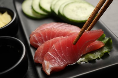 Photo of Taking tasty sashimi (piece of fresh raw tuna) from black plate at table, closeup