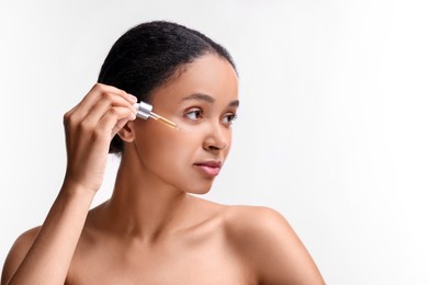 Photo of Beautiful woman applying serum onto her face on white background. Space for text