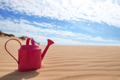 Photo of Pink watering can on sand in desert. Space for text