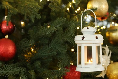 Christmas lantern with burning candle on fir tree as background, closeup