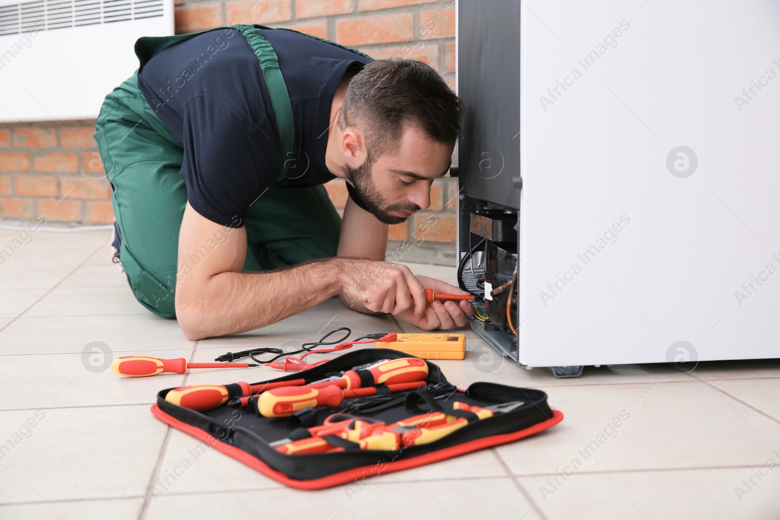 Photo of Male technician in uniform repairing refrigerator indoors