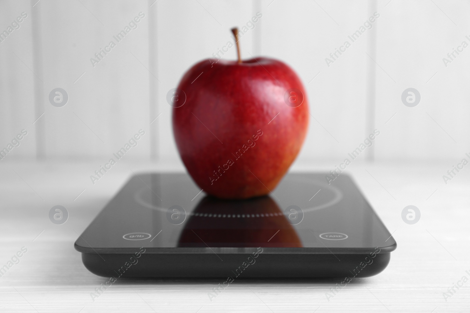 Photo of Digital kitchen scale with ripe red apple on white wooden table