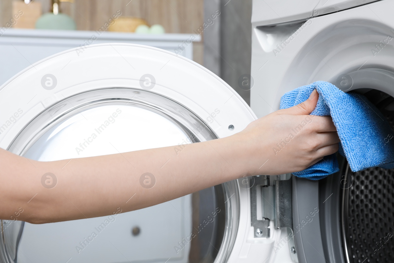 Photo of Woman cleaning washing machine with rag indoors, closeup