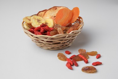 Wicker basket with different dried fruits on white background