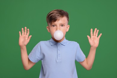 Photo of Surprised boy blowing bubble gum on green background