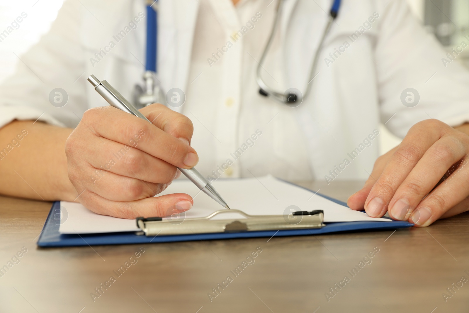 Photo of Doctor writing at wooden table, closeup view