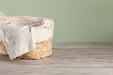 Photo of Wicker laundry basket with clothes near light green wall. Space for text