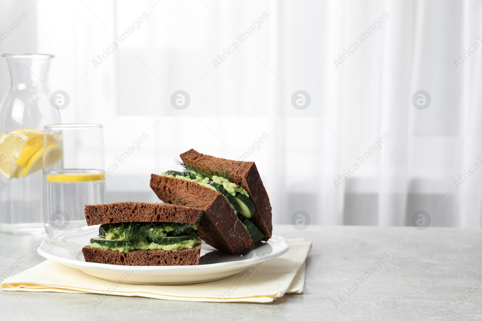 Photo of Tasty sandwiches with cucumber, cream cheese, dill and lemon water on grey table indoors, space for text