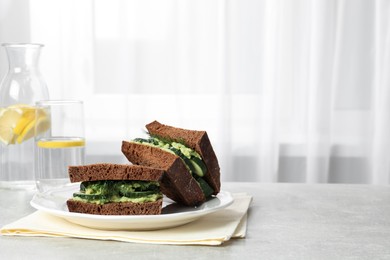 Photo of Tasty sandwiches with cucumber, cream cheese, dill and lemon water on grey table indoors, space for text