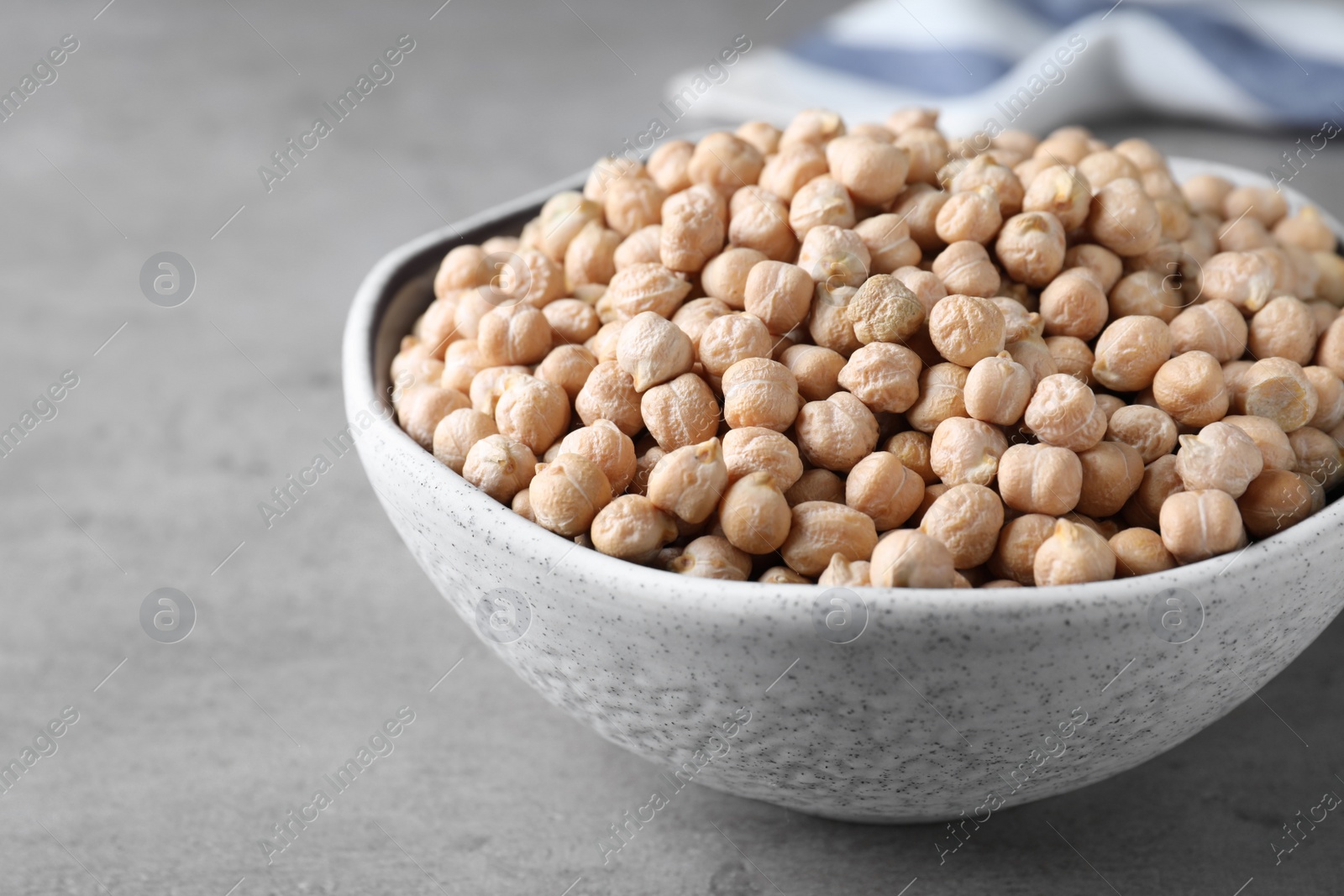 Photo of Raw chickpeas in bowl on grey table, closeup